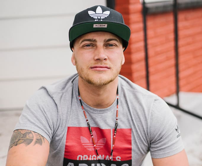 Person with a short beard, wearing a black baseball cap and light gray t-shirt looking at the camera.